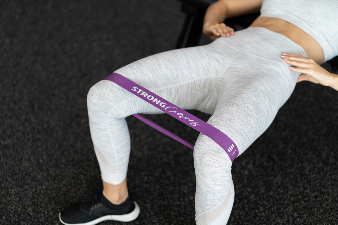 A close up of Shelley Darlington performing a hip thrust with a purple Strong Curves booty band around her knees