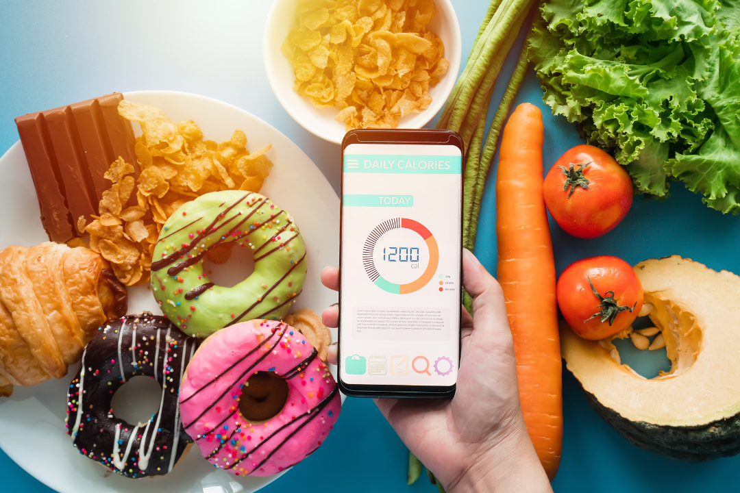 A close up of a calorie tracking app on a phone with a selection of foods in the background