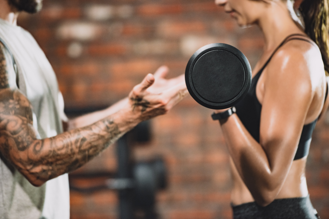 A close up of a man spotting a woman doing bicep curls