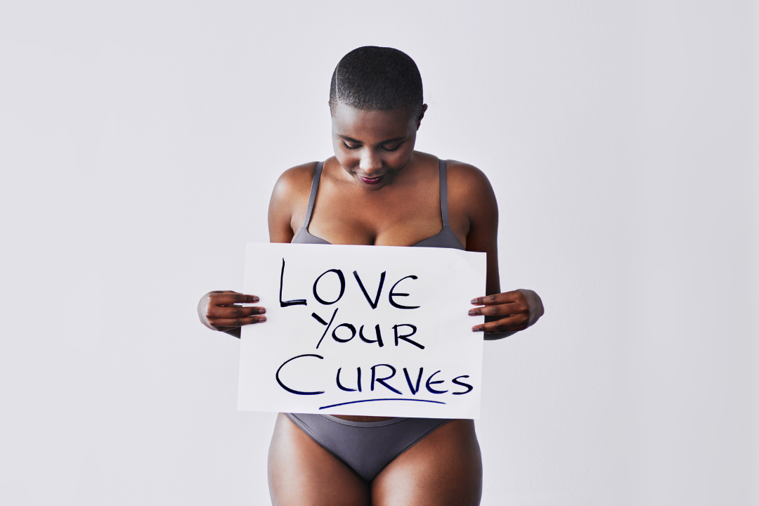 A woman in underwear holding a sign that says 'love your curves'