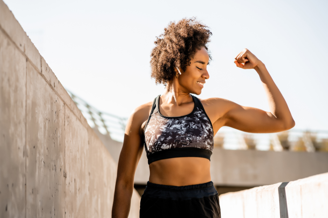 A woman in activewear outside flexing her bicep